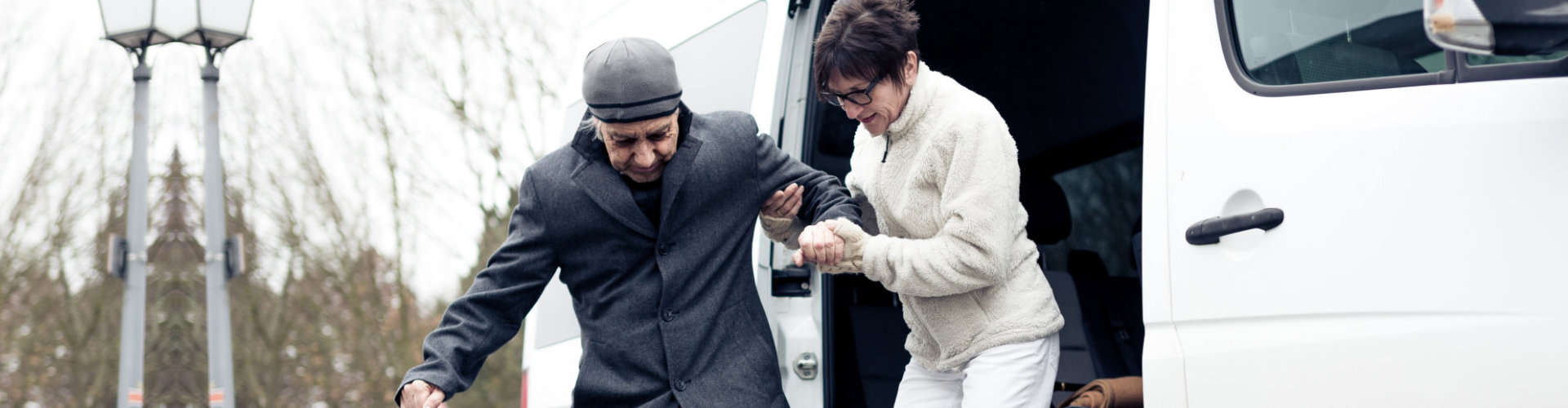 woman assisting elderly man getting out from van